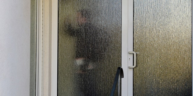 A customs officer walks behind a glass door of a house with a doctor's office during a doping raid in Erfurt, Germany, Wednesday, Feb. 27, 2019. Several people were arrested in doping raids in Austria and Germany during the Nordic skiing world championships.