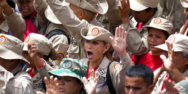 Members of the Bolivarian Militia raise their hands swearing allegiance to the fatherland during an "anti-intervention" march coinciding with the anniversary of the deadly 1989 social uprising against neoliberal measures known as the Caracazo, in Caracas, Venezuela, Wednesday, Feb. 27, 2019. (AP Photo/Ariana Cubillos)
