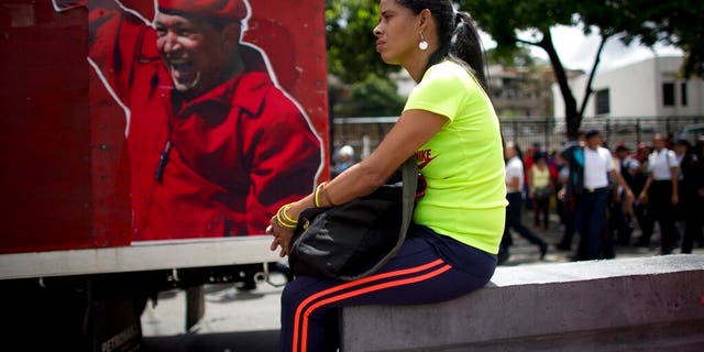 A supporter of Venezuela's President Nicolas Maduro sits next to an image depicting the late president Hugo Chavez during an "anti-intervention" march coinciding with the anniversary of the deadly 1989 social uprising against neoliberal measures known as the Caracazo, in Caracas, Venezuela, Wednesday, Feb. 27, 2019. (AP Photo/Ariana Cubillos)