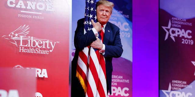 President Donald Trump hugs the American flag as he arrives to speak at Conservative Political Action Conference.