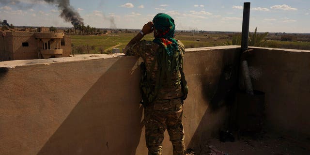 A U.S.-backed Syrian Democratic Forces (SDF) fighter watches black smoke billow from the last small piece of territory held by Islamic State militants as U.S. backed fighters pounded the area with artillery fire and occasional airstrikes in Baghouz, Syria, Sunday, March 3, 2019. (AP Photo/Andrea Rosa)