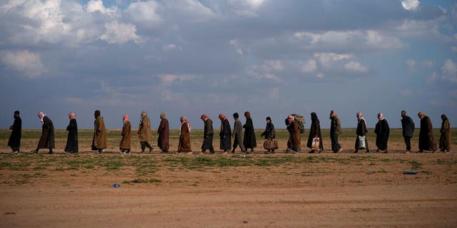 In this Friday, Feb. 22 file photo, men walk to be screened after being evacuated out of the last territory held by Islamic State group militants, near Baghouz, eastern Syria