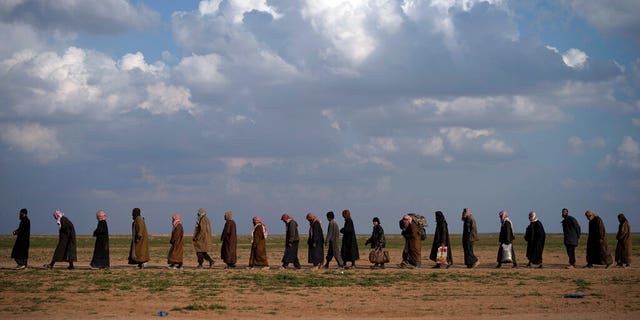 In this Friday, Feb. 22 file photo, men walk to be screened after being evacuated out of the last territory held by Islamic State group militants, near Baghouz, eastern Syria