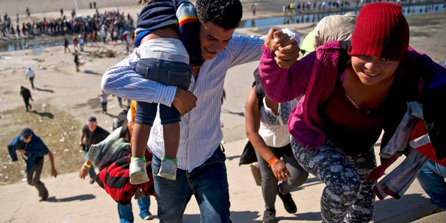 FILE - In this Nov. 25, 2018 file photo, migrants walk up a riverbank at the Mexico-U.S. border after getting past a line of Mexican police at the Chaparral border crossing in Tijuana, Mexico, as they try to reach the U.S. (AP Photo/Ramon Espinosa, File)