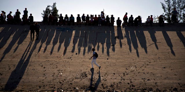 FILE - This Nov. 25, 2018 file photo shows migrants near the Chaparral border crossing watch clashes with U.S. border agents, seen from Tijuana, Mexico. A San Diego TV station says the U.S. government ran an operation to screen journalists, activists and others while investigating last year's migrant caravan from Mexico. KNSD-TV says documents leaked by a Homeland Security source show a January database listing at least 10 journalists, seven of them U.S. citizens, as warranting secondary screening at U.S. points of entry. (AP Photo/Ramon Espinosa, File)