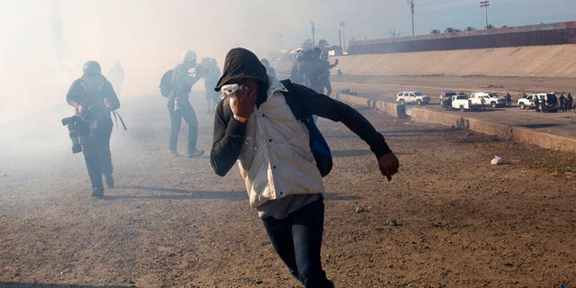 FILE - In this Nov. 25, 2018 file photo, a migrant runs from tear gas launched by U.S. agents, amid members of the press covering the Mexico-U.S. border, after a group of migrants got past Mexican police at the Chaparral crossing in Tijuana, Mexico. (AP Photo/Rodrigo Abd, File)