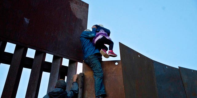 In this Dec. 2, 2018 file photo, a Honduran migrant helped a young girl cross to the U.S. side of the border wall, in Tijuana, Mexico. (AP Photo/Ramon Espinosa, File)