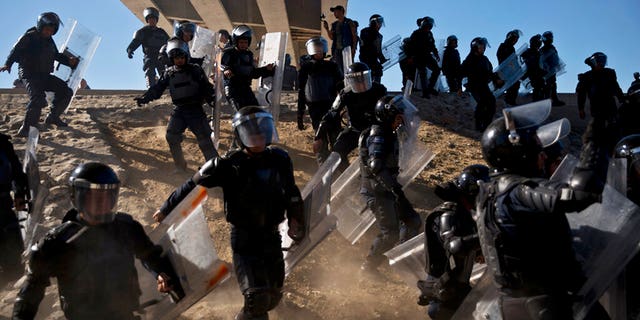 FILE - In this Nov. 25, 2018 file photo, Mexican police run as they try to keep migrants from getting past the Chaparral border crossing in Tijuana, Mexico, near San Ysidro, Calif. (AP Photo/Ramon Espinosa, File)