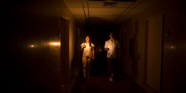 Relatives of a patient walk in the darkened hall of a clinic with a candle lighting the way, during a power outage in Caracas.