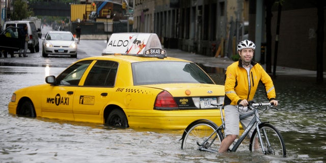 FILE - In this Aug. 28, 2011 file photo, a bicyclist makes his way past a stranded taxi on a flooded New York City street as Tropical Storm Irene passes through the city. (AP Photo/Peter Morgan, File)