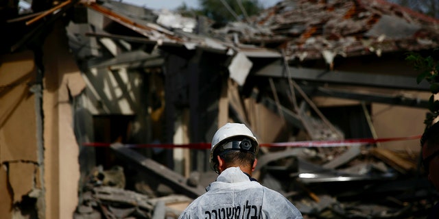 An Israeli police officer inspects the damage to a house hit by a rocket in Mishmeret, central Israel, Monday, March 25, 2019. An early morning rocket from the Gaza Strip struck a house in central Israel on Monday, wounding several people, including one moderately, an Israeli rescue service said, in an eruption of violence that could set off another round of violence shortly before the Israeli election. (AP Photo/Ariel Schalit)