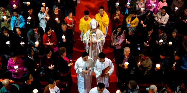 FILE - In this Saturday, March 31, 2018, file photo, Chinese Bishop Joseph Li Shan, center, walks down the aisle during a Holy Saturday Mass on the evening before Easter at the Cathedral of the Immaculate Conception, a government-sanctioned Catholic church in Beijing. (AP Photo/Mark Schiefelbein, File)