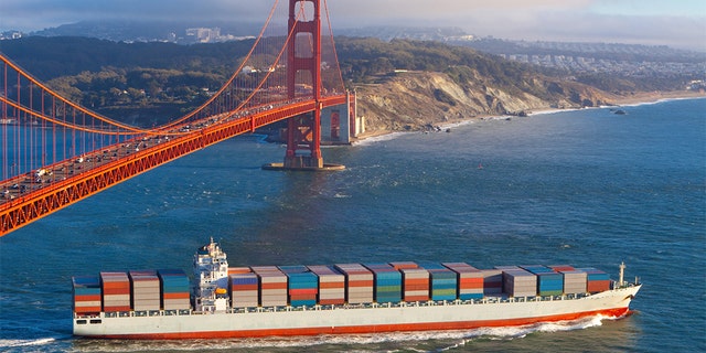 Full container cargo ship sailing out of San Francisco bay under the Golden gate bridge and heading out into the Pacific Ocean in the late afternoon