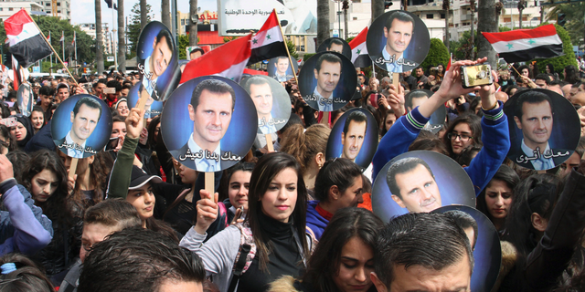 In this photo released by the Syrian official news agency SANA, people hold Syrian flags and portraits of President Bashar Assad during a protest against U.S. President Donald Trump's move to recognize Israeli sovereignty over the Israeli occupied Golan Heights, in the costal port city of Tartus, Syria, Wednesday, March. 27, 2019. (SANA via AP)