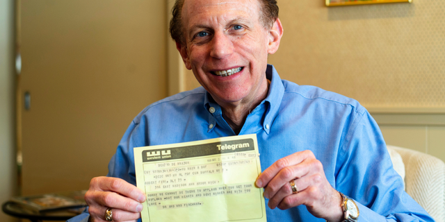 In a Friday, March 1 2019 photo, Robert Fink holds up a telegram from a family friend congratulating him on his 1969 graduation from the University of Michigan at his home in Huntington Woods, Mich. The telegram, delivered to his apartment the day after he moved away from Ann Arbor, was recovered 50 years later by an employee of a downtown Ann Arbor company in a filing cabinet bought from the University of Michigan. (Jacob Hamilton/Ann Arbor News via AP)