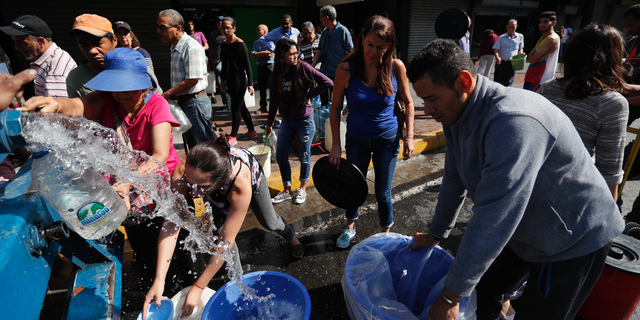 People collect water from a truck that delivers water during rolling blackouts, in Caracas, Venezuela, Tuesday, March 12, 2019.