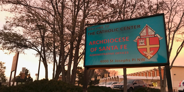FILE - In this Nov. 29, 2018, file photo, the sun sets on a sign in front of the Archdiocese of Santa Fe offices in Albuquerque, N.M. A priest who fled the United States decades ago faces a federal trial on charges that he sexually abused a New Mexico boy in the early 1990s at an Air Force base and veterans' cemetery. Arthur Perrault, a one-time pastor in Albuquerque, has been charged with aggravated sexual abuse and others counts. (AP Photo/Susan Montoya Bryan, File)