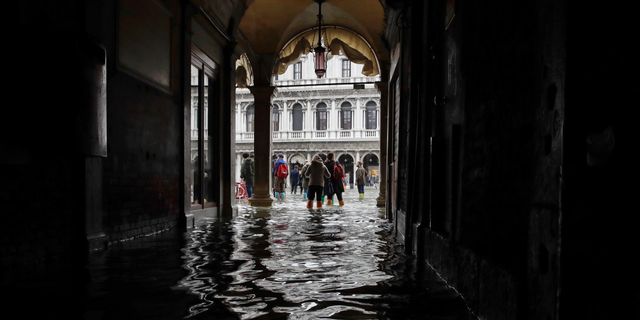 FILE - In this Thursday, Nov. 1, 2018 file photo, tourists walk in the flooded St. Mark's Square in Venice, Italy, as rainstorms and strong winds hit the area. On Thursday, March 28, 2019, the United Nations’ weather agency says extreme weather in 2018 hit 62 million people worldwide last year and created 2 million refugees as man-made climate change worsened. (AP Photo/Luca Bruno)