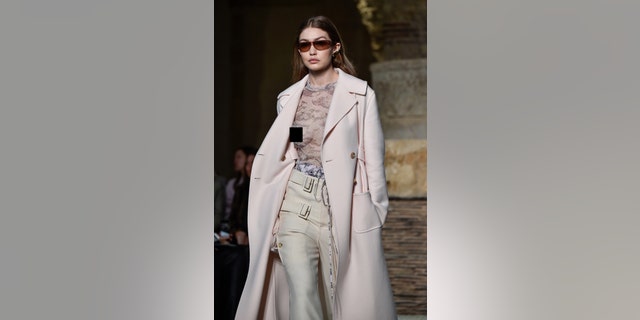 Gigi dons a sheer top and light pink coat