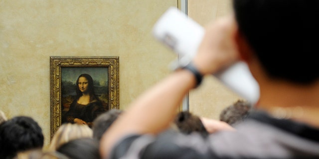 A tourist takes souvenir photos of Italian painter Leonardo da Vinci's famed portrait Mona Lisa at the Louvre Museum in Paris, Aug. 12, 2009.