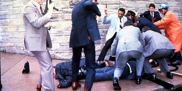FILE - James Brady and a police officer are seen lying on the ground after being shot while the suspect John Hinckley Jr. is apprehended, at right, moments after the attempted assassination of President Ronald Reagan, Washington, DC, March 30, 1981. (Photo by Dirck Halstead/Getty Images)