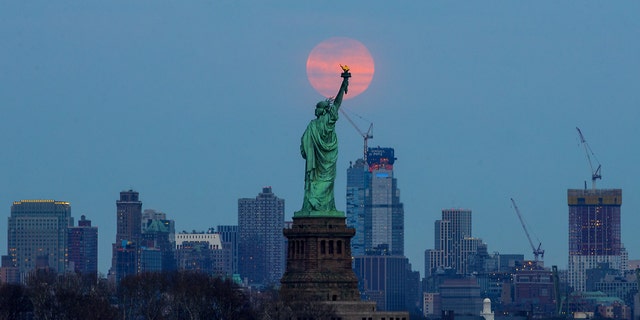 The last supermoon of 2019 rises behind the Statue of Liberty in New York, United States, on March 20, 2019.