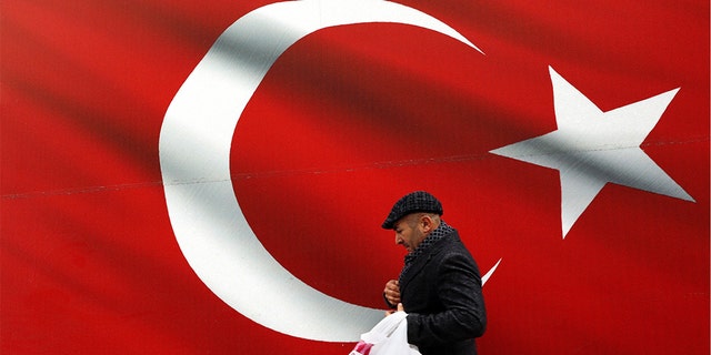 A man walking by a giant Turkish flag in Ankara, Turkey, on Sunday. Turkish citizens have begun casting votes in municipal elections for mayors, local assembly representatives and neighborhood or village administrators. (AP Photo/Ali Unal)