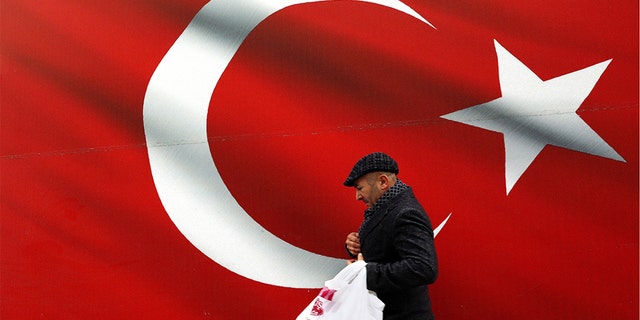 A man walking by a giant Turkish flag in Ankara, Turkey, on Sunday. Turkish citizens have begun casting votes in municipal elections for mayors, local assembly representatives and neighborhood or village administrators. (AP Photo/Ali Unal)