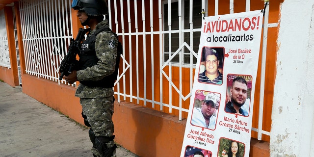 A Civil Forces police officer stands next to a banner with pictures of five youngsters who went missing January 11, 2016, in Tierra Blanca community, Veracruz State, Mexico.