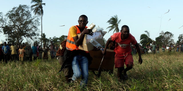 March 28, 2018: Community members assist a doctor carrying boxes with medical supplies as he runs towards the South African Defence Forces helicopter after assisting a community affected by a cyclone near Beira, Mozambique.