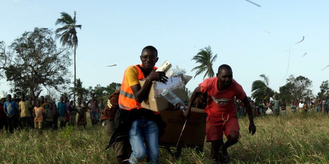 March 28, 2018: Community members assist a doctor carrying boxes with medical supplies as he runs towards the South African Defence Forces helicopter after assisting a community affected by a cyclone near Beira, Mozambique.
