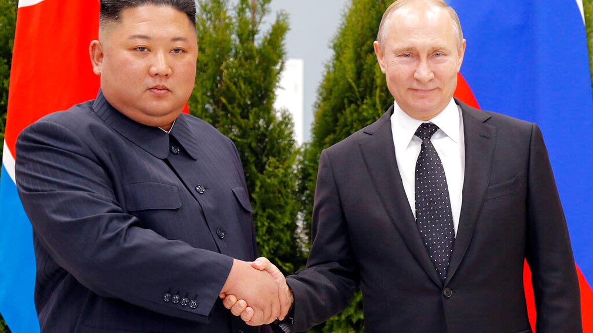 Russian President Vladimir Putin in a suit shakes hands with North Korean Dictator Kim Jong Un