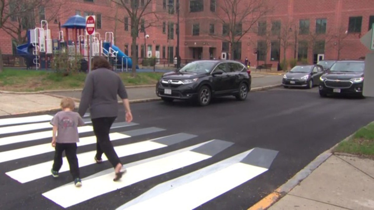 A pedestrian walks across the newly designed 3D crosswalk. The walkway was designed by a pair of fourth graders in Massachusetts.