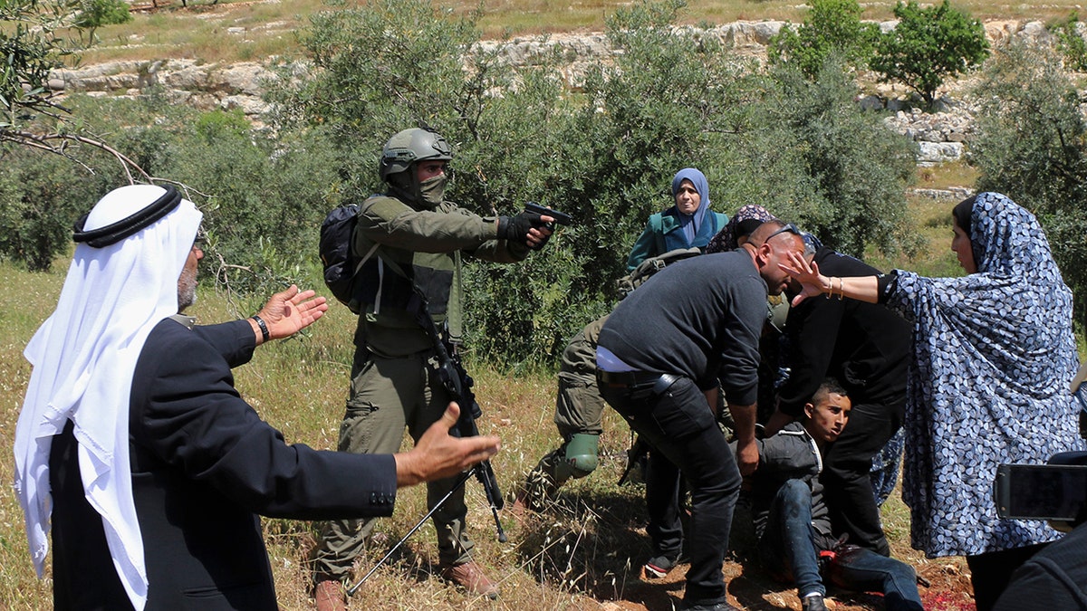 An Israeli soldier points his pistol at a group of Palestinians gathering around a wounded Osama Hajahjeh, 16, near the village of Tekoa, West Bank. (AP Photo/Mustafa Allbadan)