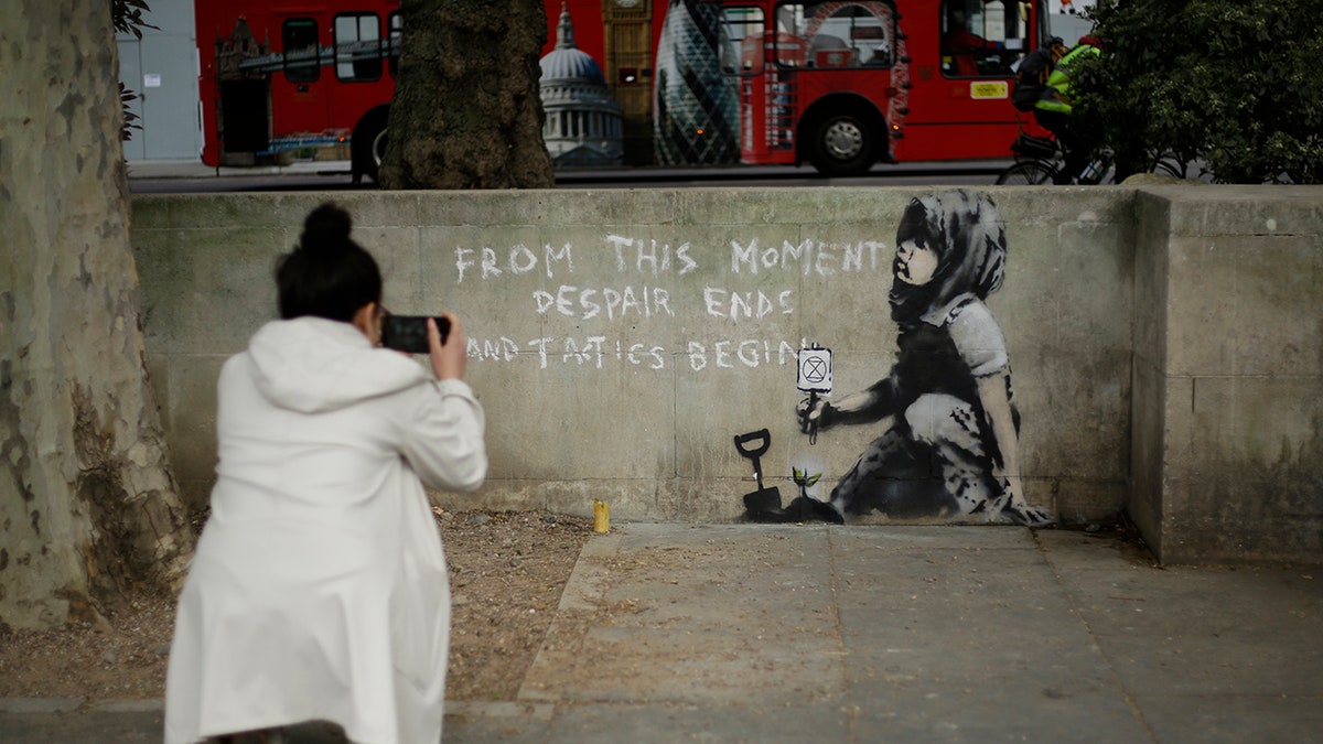 A woman takes a picture of a new piece of street art that people noticed for the first time last night and is believed to be by street artist Banksy on a wall where Extinction Rebellion climate protesters had set up a camp in Marble Arch, London, Friday, April 26, 2019.?