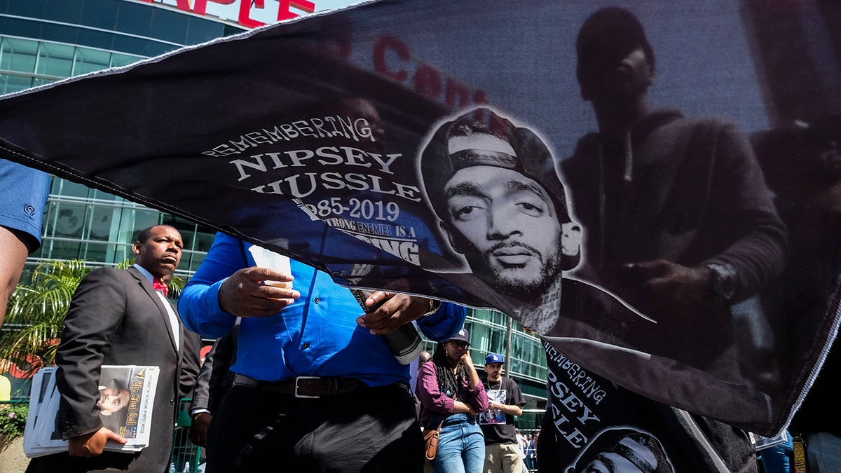 A fan of rapper Nipsey Hussle holds a flag with Hussle's image on it as he attends a public memorial at Staples Center in Los Angeles, Thursday, April 11, 2019. (AP Photo/Ringo H.W. Chiu)