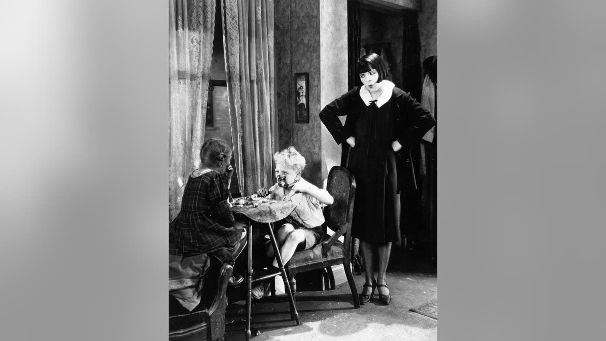 1926: Silent film star Colleen Moore (1900 - 1988) despairs at the table manners of two mucky children in a scene from the film "Irene," directed by Alfred E Green for First National. The girl is child actress Fay McKenzie and the boy is Bobby Lloyd. —  Photo by Hulton Archive/Getty Images