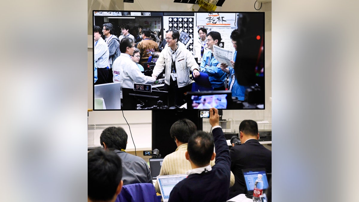 Members of The Japan Aerospace Exploration Agency, or JAXA, seen on screen, celebrate, as Hayabusa2 spacecraft safely evacuated and remained intact after the blast, in Sagamihara, near Tokyo, Friday, April 5, 2019.