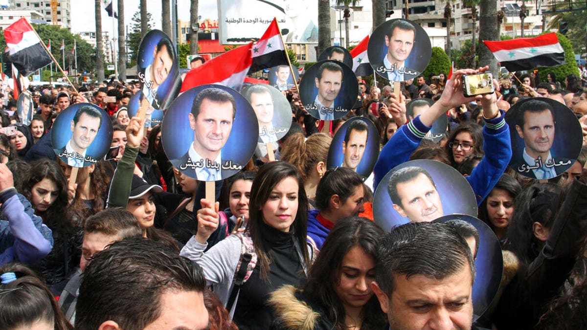 In this photo released by the Syrian official news agency SANA, people hold Syrian flags and portraits of President Bashar Assad during a protest against U.S. President Donald Trump's move to recognize Israeli sovereignty over the Israeli occupied Golan Heights, in the coastal port city of Tartus, Syria, Wednesday, March. 27, 2019.