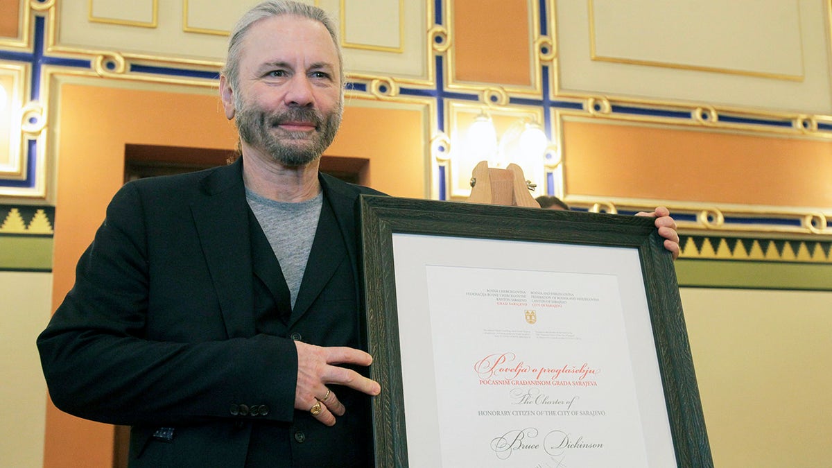 Bruce Dickinson poses for cameras with his honorary citizen certificate at the city hall in Sarajevo, Bosnia-Herzegovina, Saturday, April 6, 2019. Bosnia's capital Sarajevo has declared Iron Maiden lead singer Bruce Dickinson an honorary citizen in gratitude for the concert the heavy metal band held while the city was under siege during 1992-95 war. (AP Photo/Eldar Emric)