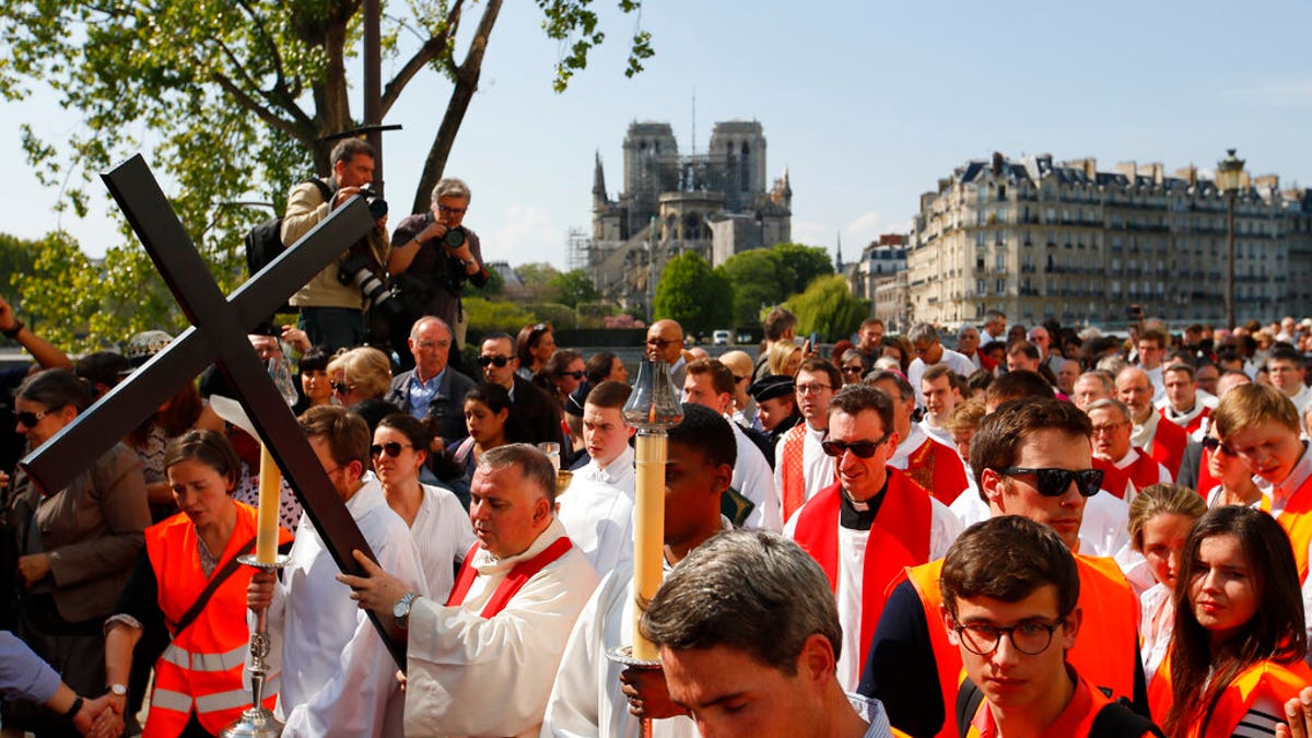 With Notre Dame cathedral in background, religious officials carry the cross during the Good Friday procession, Friday, April 19, 2019 in Paris.