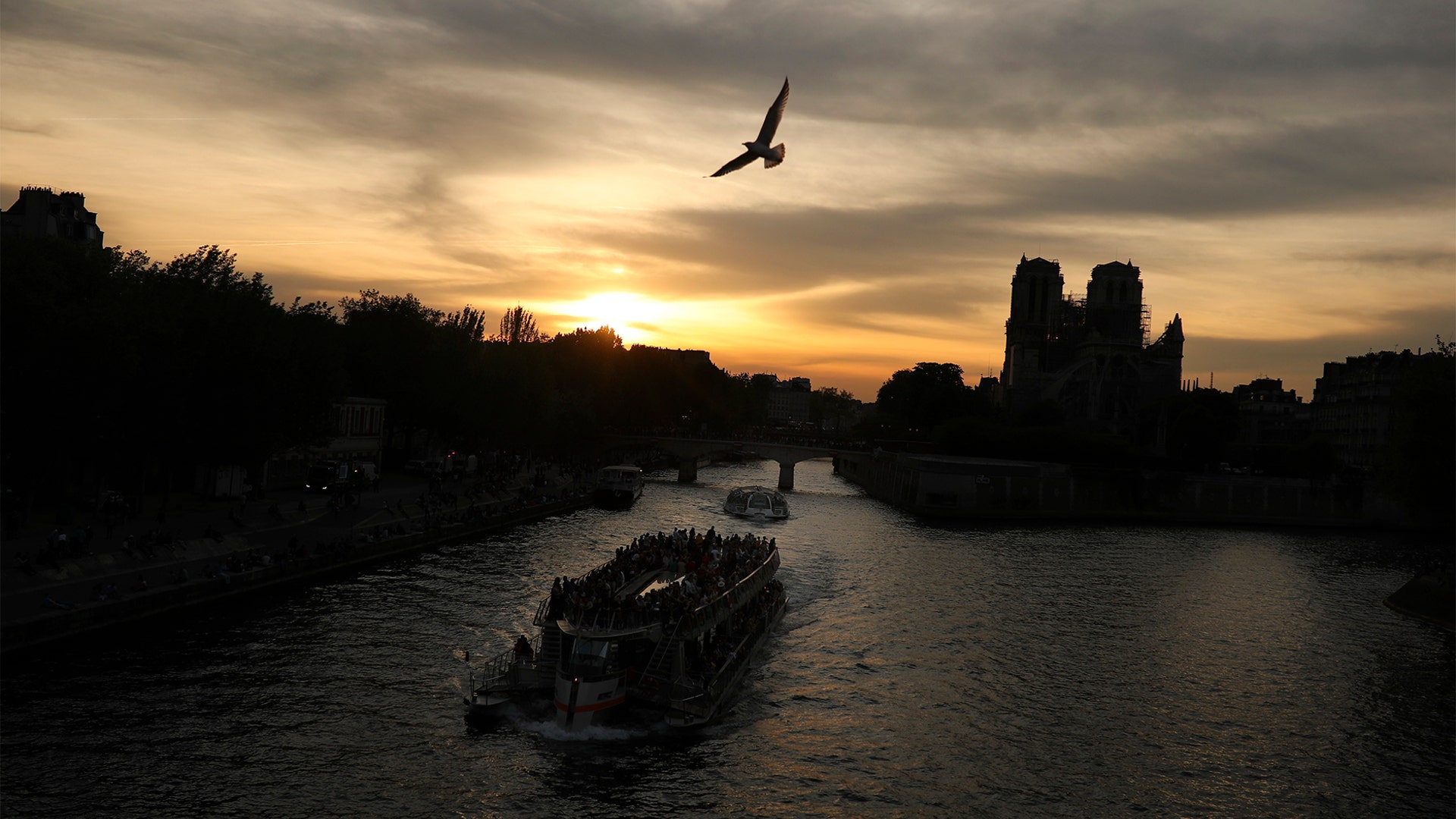 Boats sail along the Seine river next to the Notre Dame Cathedral as the sun sets in Paris, April 21, 2019. 