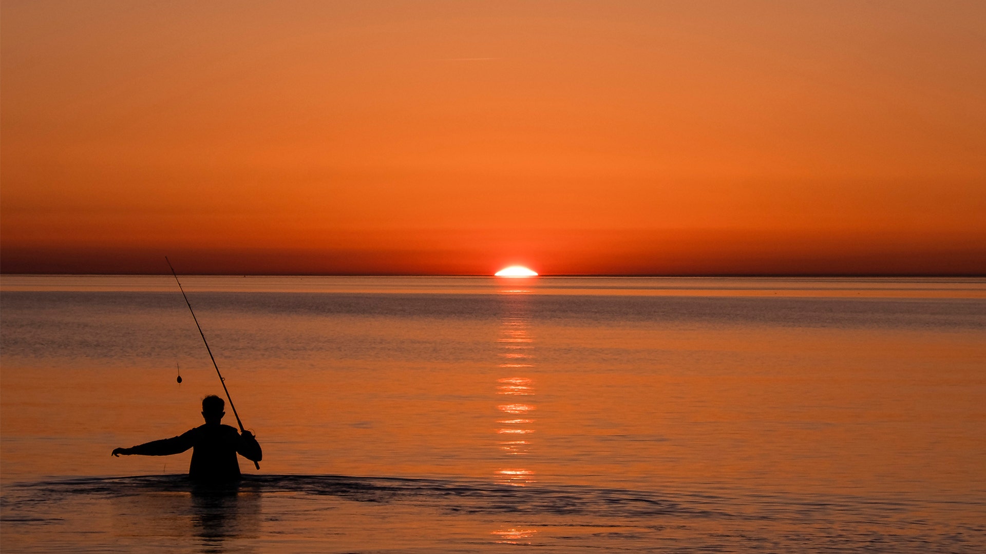 An angler goes into the water at sunset in Fl'gge, Germany, April 21, 2019. 