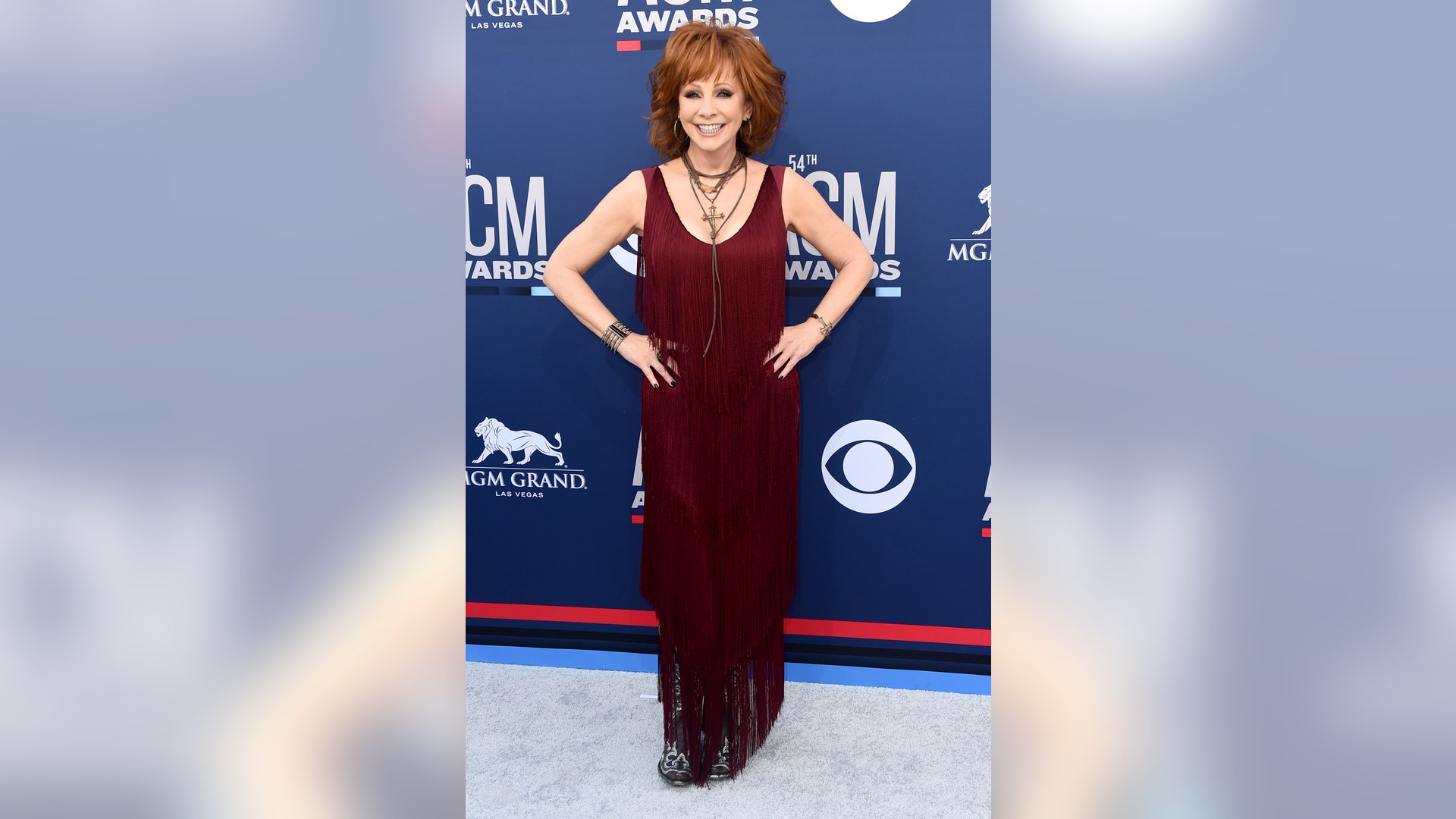 Reba McEntire hits the carpet in a burgundy dress with fringe detailing before she takes the 2019 ACM Awards stage to host one of country music's biggest nights.