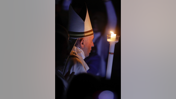 Pope carries Easter candle up aisle of darkened basilica