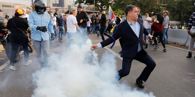 An opponent to Venezuela's President Nicolas Maduro returns a tear gas canister in Caracas, Venezuela, on Monday.