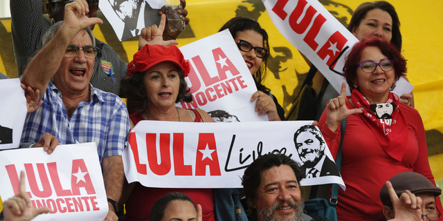 ADDS DA SILVA'S SENTENCE REDUCTION - Supporter of Brazil's former President Luiz Inacio Lula da Silva, holds signs with text that reads in Portuguese "Free Lula" and "Lula Innocent" during a vigil in front of the headquarters of the Superior Court of Justice, in Brasilia, Brazil, Tuesday, April 23, 2019. Da Silva, who was found guilty of passive corruption and money laundering, has been in jail since April of last year. Brazil’s second highest court is reducing the sentence of incarcerated ex-president Luis Inacio Lula da Silva from 12 years and one month to eight years and 10 months. (AP Photo/Eraldo Peres)