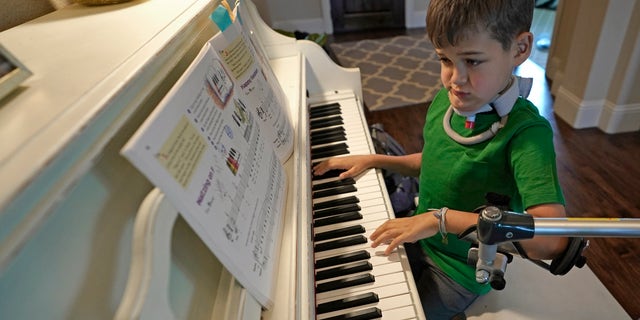 Braden Scott, who was diagnosed with AFM, uses a device to support his left arm as he practices on the piano in Tomball, Texas.