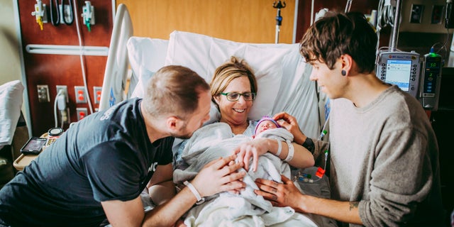 Matthew Eledge, left, his mother Cecile Eledge, center, and Matthew's husband Elliot Dougherty, right, greet baby Uma after her delivery at the Nebraska Medical Center in Omaha, Neb.