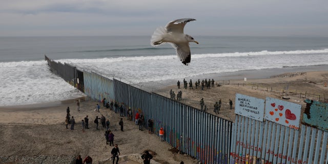 FILE - In this Dec. 10, 2018, file photo, people look on from the Mexican side, left, as U.S. Border Patrol agents on the other side of the U.S. border wall in San Diego prepare for the arrival of hundreds of pro-migration protestors, seen from Tijuana, Mexico. The southern border is nearly 2,000 miles long and already has about 650 miles of different types of barriers, including short vehicle barricades and tall, steel fences that go up to 30 feet high. (AP Photo/Rebecca Blackwell, File)